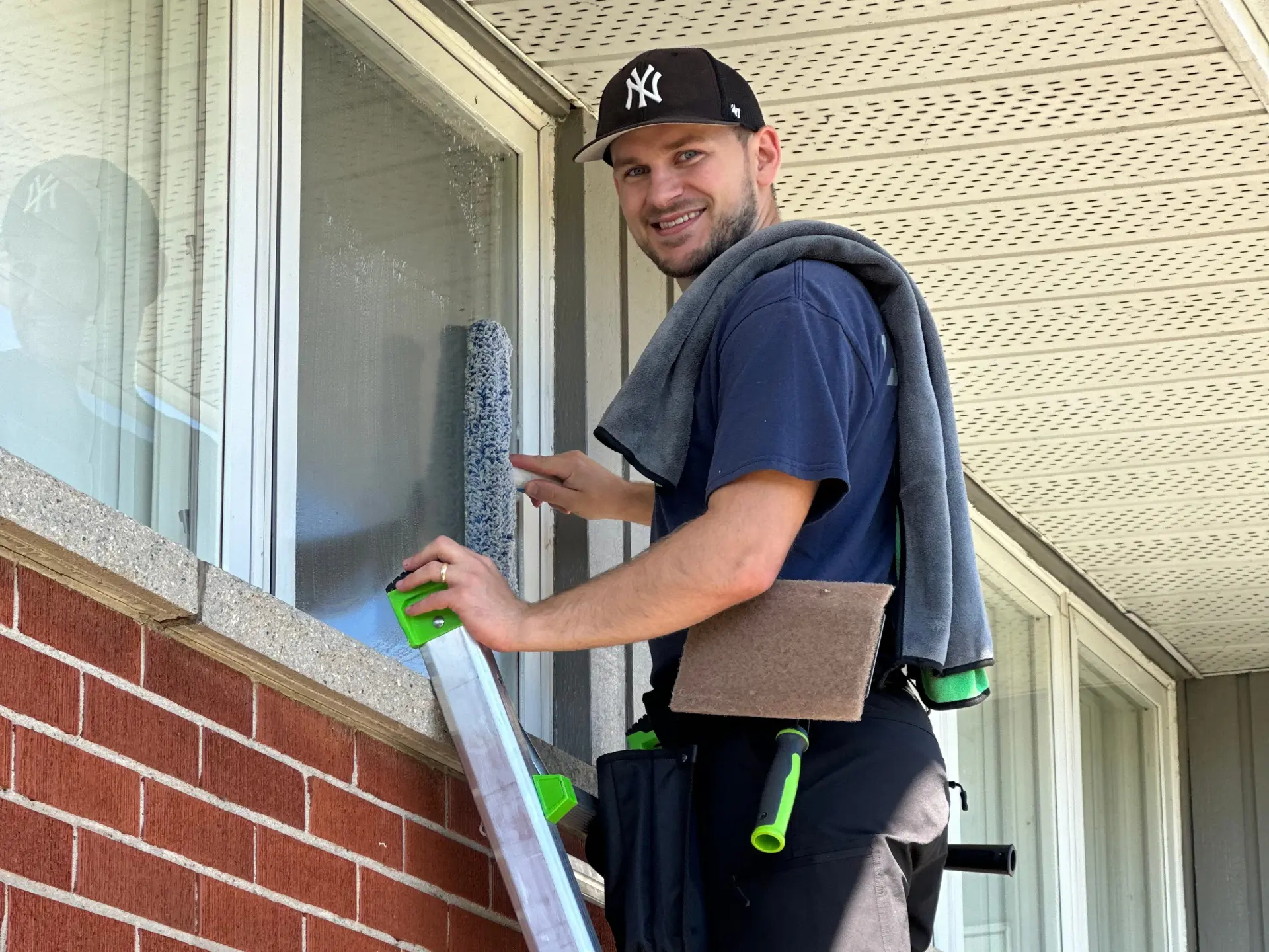 A Daylight Window Cleaning technician hand-scrubbing a residential window on a ladder for a streak-free finish in Kitchener