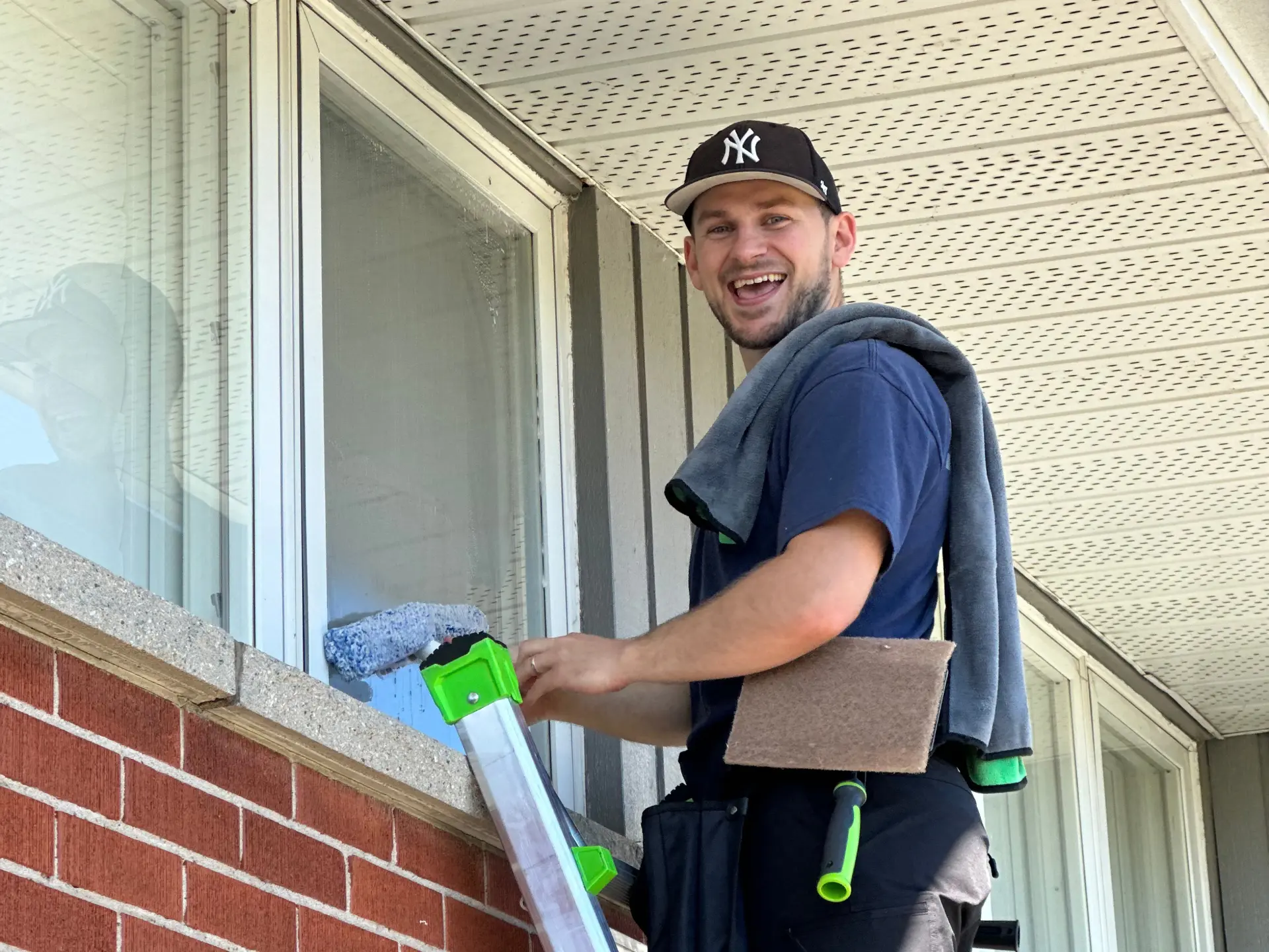 Cameron Patton, owner of Daylight Window Cleaning, hand-cleaning exterior windows on a ladder at a home in Cambridge, Ontario